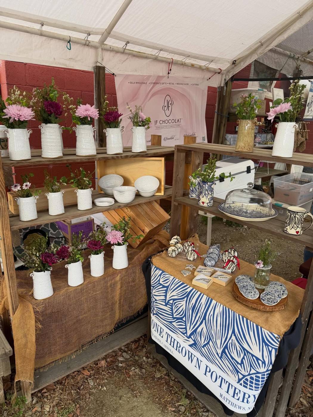 A market tent with shelves of white vases holding flowers and a table of carved pottery