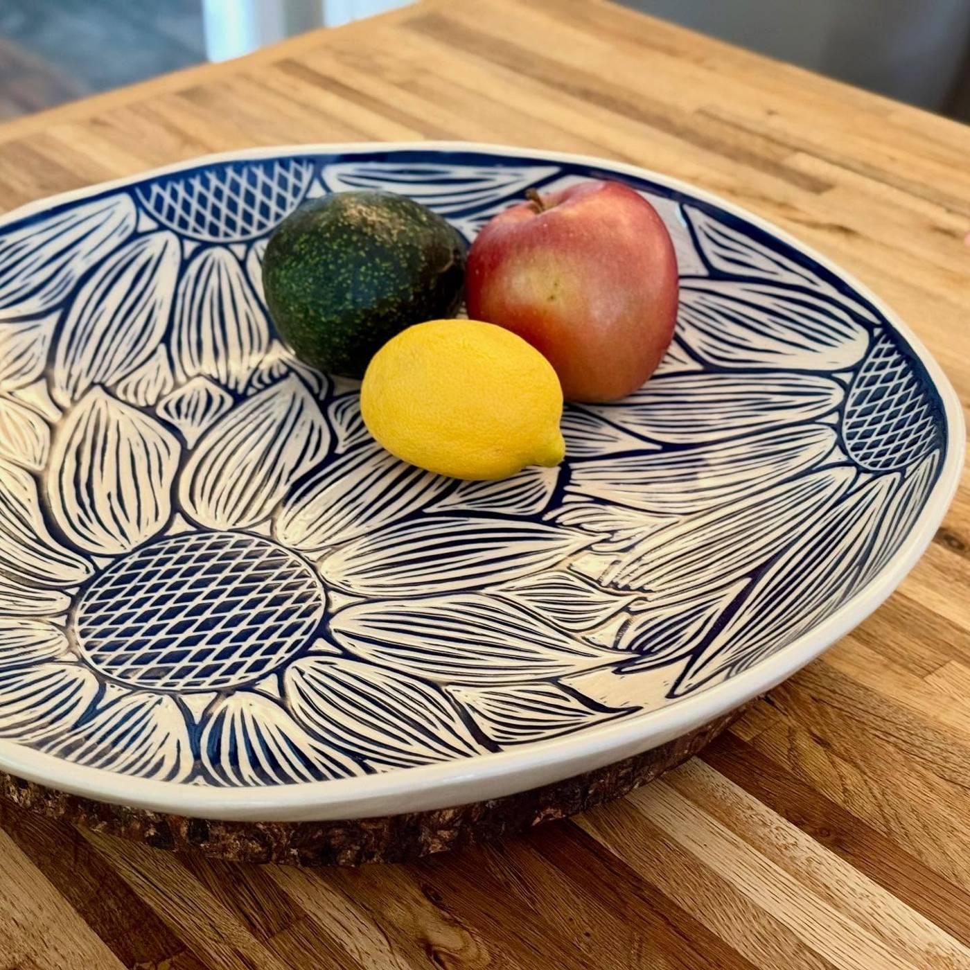 Carved sunflower platter holding an avocado, an apple and a lemon on a butcher-block counter