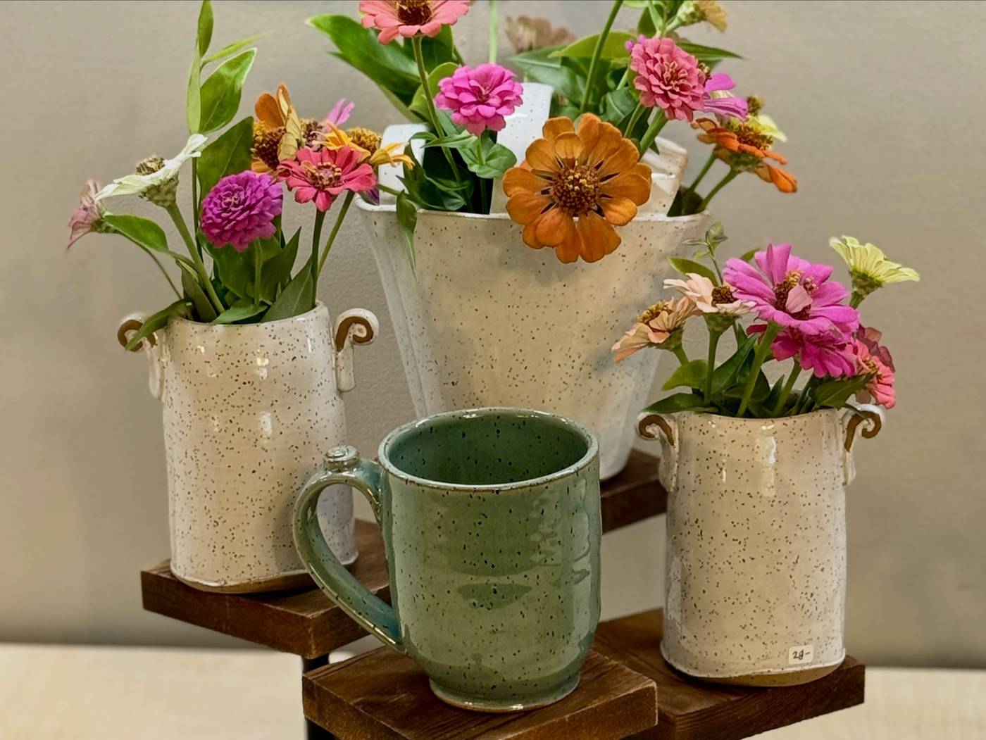 Speckled vases full of zinnias beside a green glazed mug