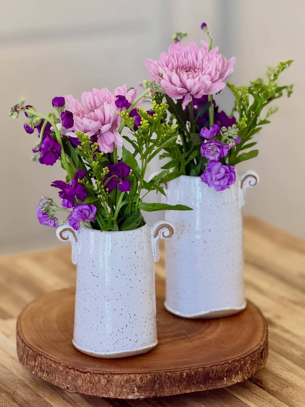 Two speckled white vases with purple and pink flowers
